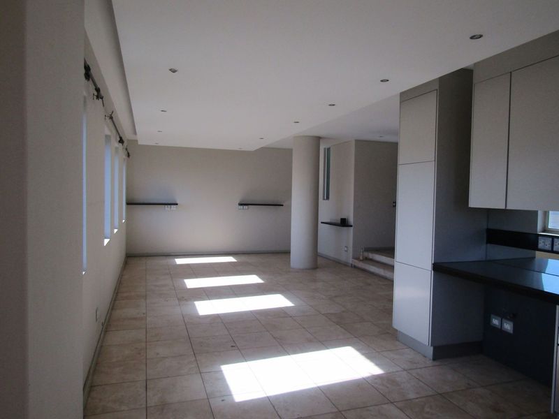 Spacious open-plan living area featuring neutral tiled flooring, recessed lighting, and a modern kitchen section with built-in cabinetry and stone countertops.