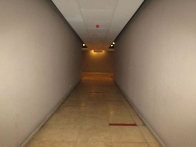 A long, empty interior hallway featuring tiled flooring and recessed ceiling lighting, providing a neutral transition space within the apartment.