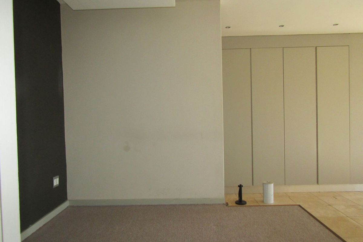 An empty bedroom featuring built-in cupboards, recessed downlighting, and a combination of carpet and tiled flooring.