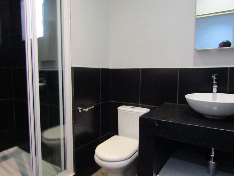 Modern bathroom featuring a shower enclosure, a white vessel sink on a black vanity counter, and a wall-mounted mirror.