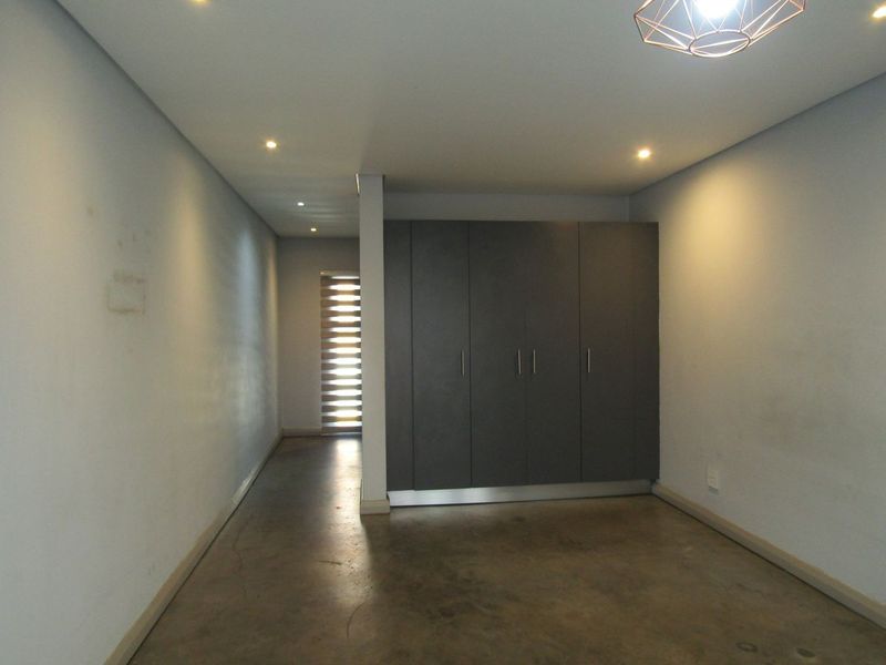 An empty bedroom featuring polished concrete flooring, built-in dark cabinetry, recessed lighting, and a window with a fitted roller blind.