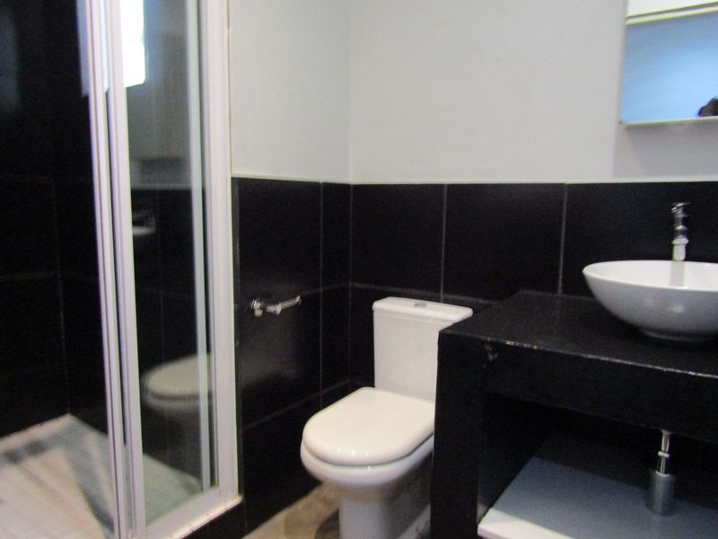 A modern bathroom featuring a shower enclosure, a white toilet, and a vessel sink set on a black vanity counter with contrasting wall tiles.