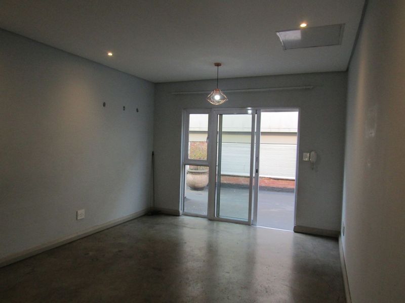 An empty living room featuring polished concrete floors, recessed lighting, and a sliding glass door providing access to an outdoor area.