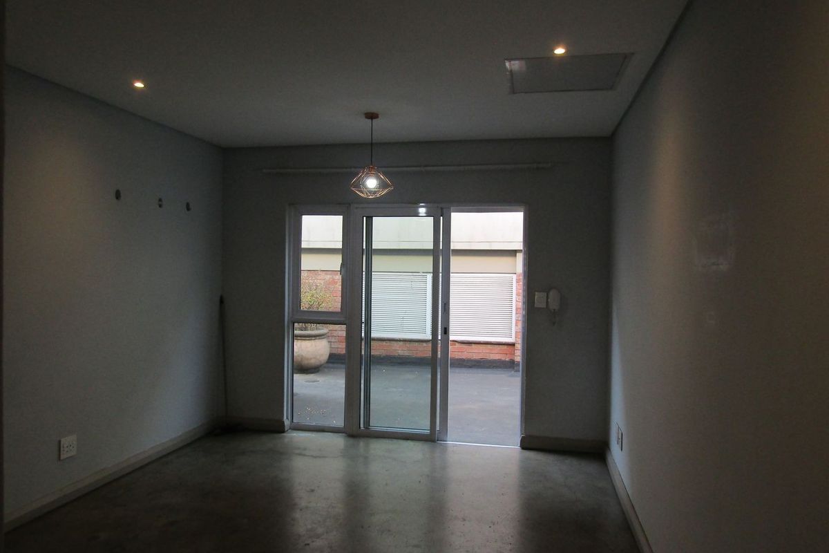 An empty living room featuring polished concrete floors, recessed lighting, and a sliding glass door providing access to an outdoor patio area.