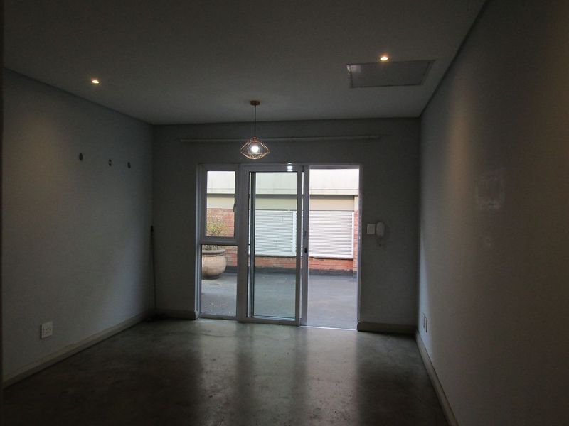 An empty living room featuring polished concrete floors, recessed lighting, and a sliding glass door providing access to an outdoor patio area.