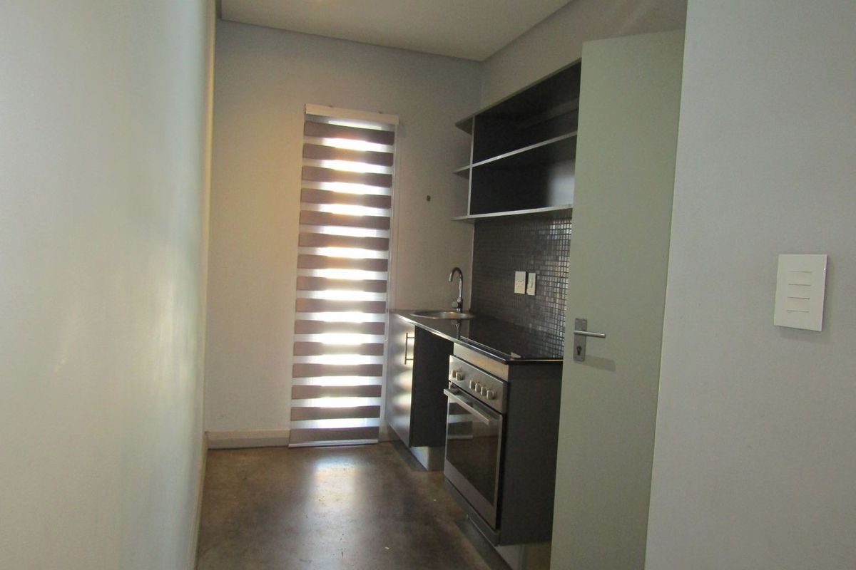 A compact, modern kitchen featuring built-in cabinetry, a built-in oven and hob, mosaic tile backsplash, and polished concrete flooring.