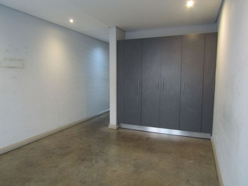 An empty bedroom featuring polished concrete flooring, recessed downlighting, and modern grey built-in cupboards.