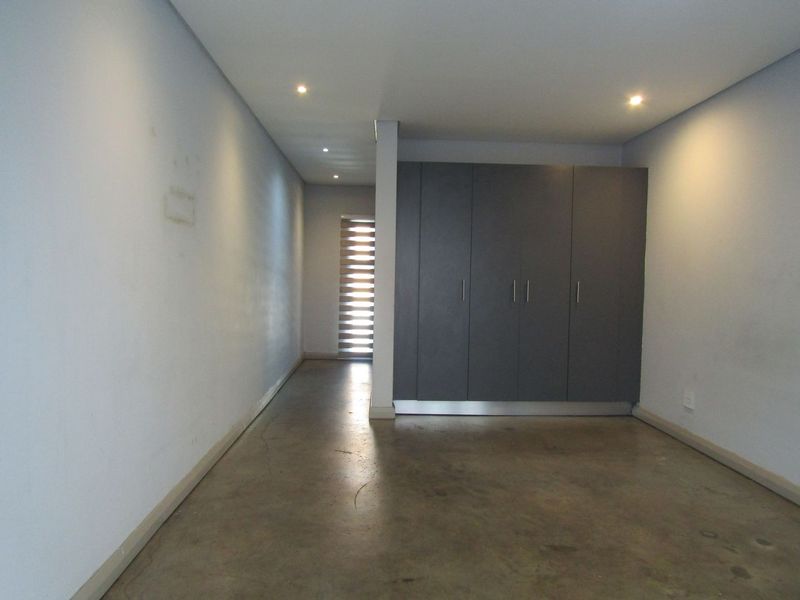 An empty bedroom featuring polished concrete flooring, built-in dark grey cabinetry, and recessed downlighting.