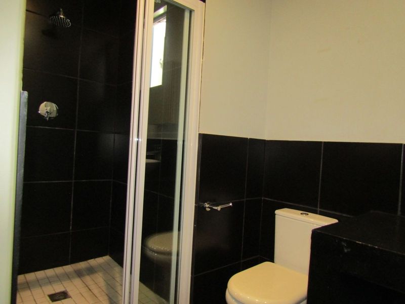 A functional bathroom featuring a shower enclosure with black wall tiles and a standard toilet.