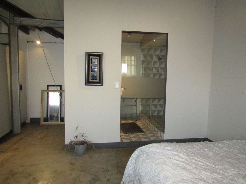 Bedroom featuring industrial-style concrete flooring, exposed steel beams, and an integrated en-suite bathroom with a glass-enclosed shower and patterned tiling.