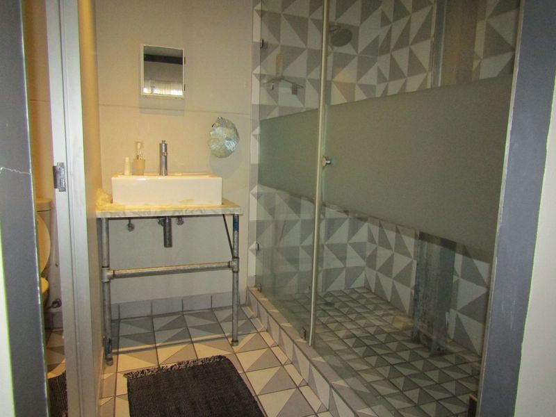 A compact bathroom featuring a modern vessel sink with an industrial-style vanity, a walk-in shower with glass enclosure, and distinctive geometric patterned tiling.