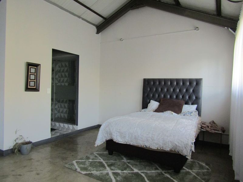 Spacious bedroom featuring vaulted ceilings with exposed rafters, polished concrete flooring, and direct access to an en-suite bathroom.