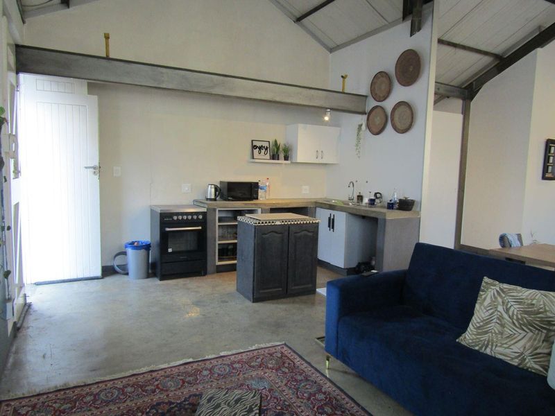 Open plan living area featuring industrial-style exposed steel beams, concrete flooring, and a functional kitchen with concrete countertops and built-in oven.