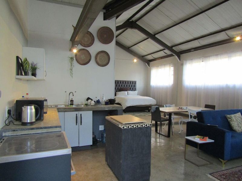 An open-plan studio apartment featuring a kitchen with concrete countertops, exposed vaulted ceiling beams, and polished concrete flooring, creating a spacious industrial-style living area.