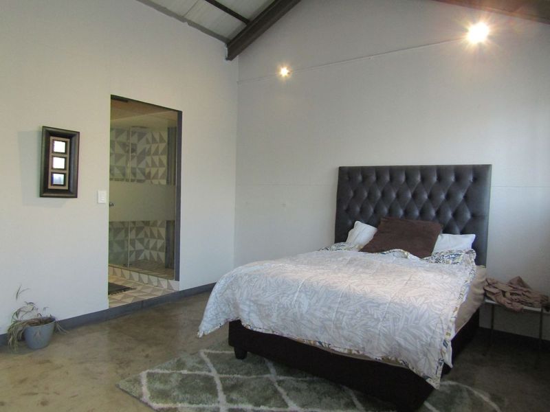 Spacious bedroom featuring polished concrete floors, exposed rafters, and direct access to an en-suite bathroom with patterned tiling.