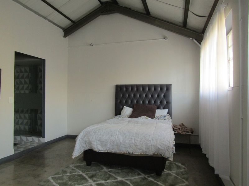 A bedroom featuring a vaulted ceiling with exposed rafters, polished concrete flooring, and direct access to an en-suite bathroom.