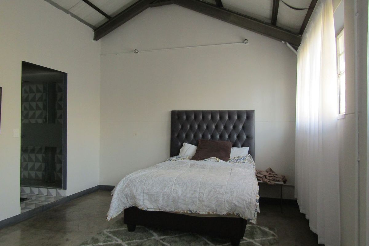 A bedroom featuring a vaulted ceiling with exposed rafters, polished concrete flooring, and direct access to an en-suite bathroom.