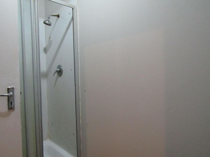 A basic bathroom shower enclosure featuring a standard shower head and mixer, showing signs of wear and dated finishes.