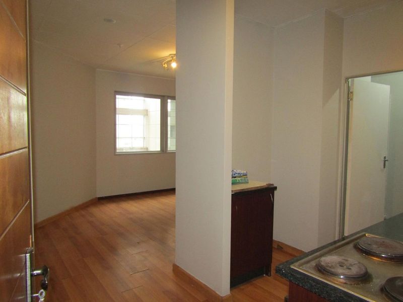 An empty open-plan living area featuring laminate flooring and a compact kitchen corner with a built-in hob.