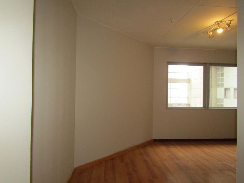 An empty living room featuring laminate flooring, neutral walls, and track lighting, offering a blank canvas for personalization.
