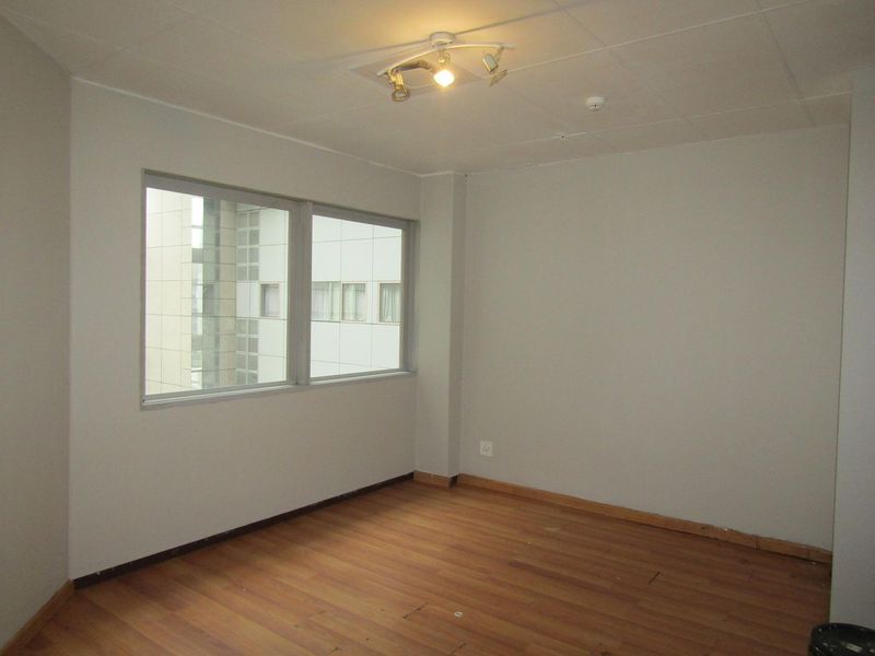 An empty bedroom featuring laminate flooring, neutral walls, and large windows providing natural light. The space is ready for personalization.