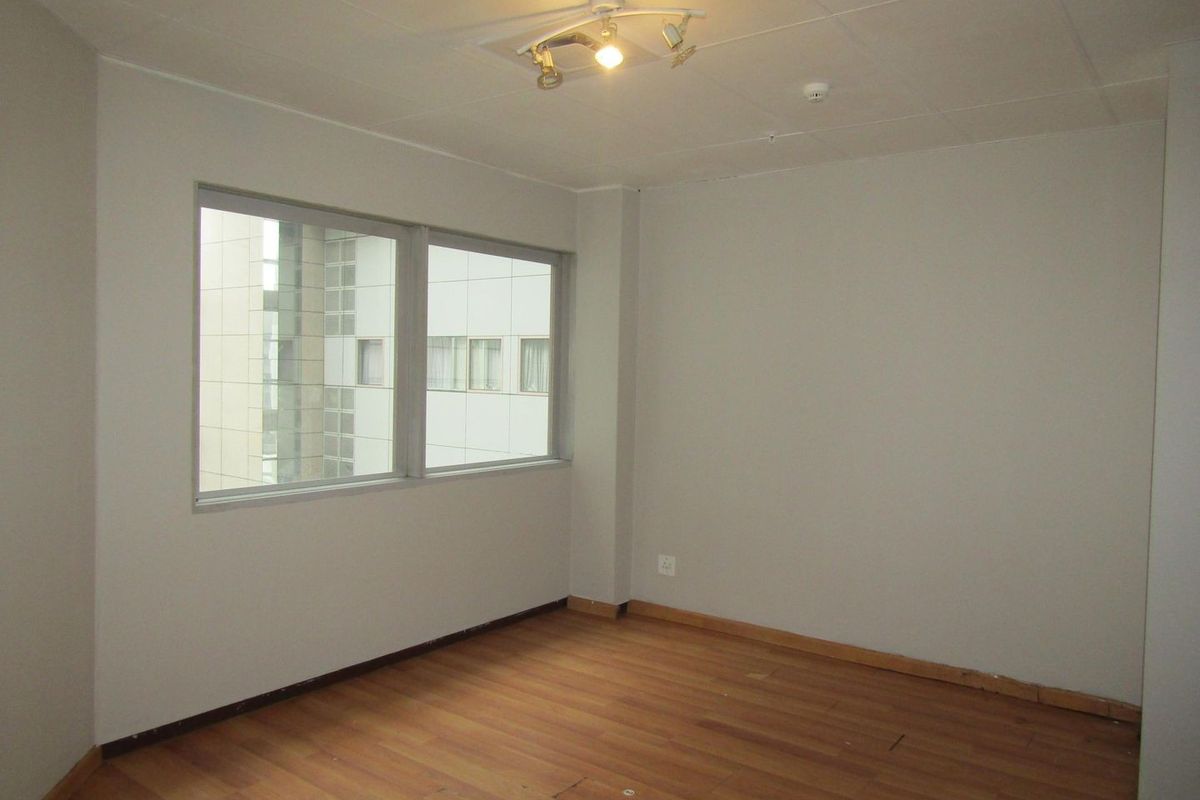 An empty bedroom featuring laminate flooring, neutral walls, and large windows providing natural light. The space is ready for personalization.