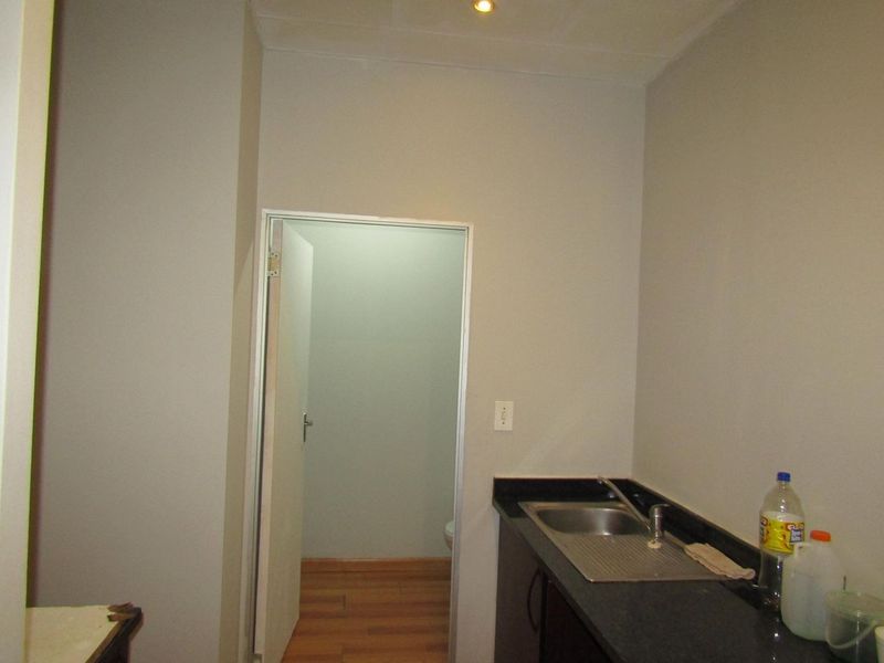 A functional scullery area featuring a stainless steel sink, dark cabinetry, and black granite countertops, with an adjacent doorway leading to another room.