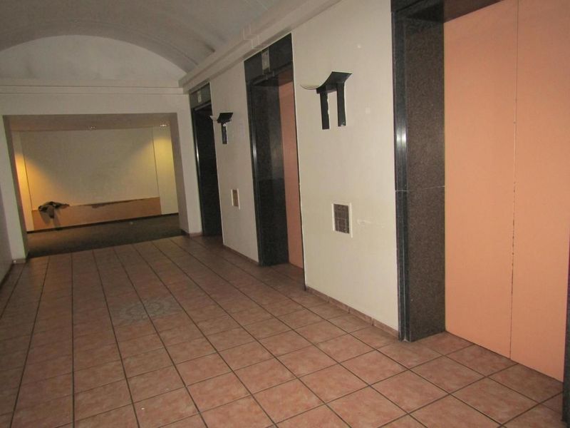 A spacious apartment building hallway featuring tiled flooring, a vaulted ceiling, and multiple elevator access points.