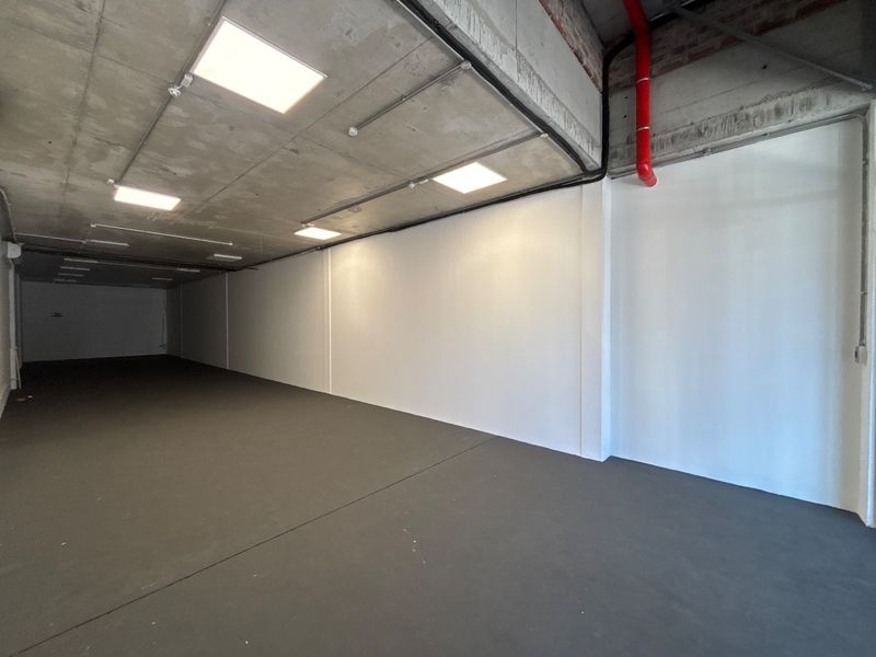A spacious, modern open-plan retail unit featuring an industrial aesthetic with exposed concrete ceilings, recessed lighting, and clean, painted walls.