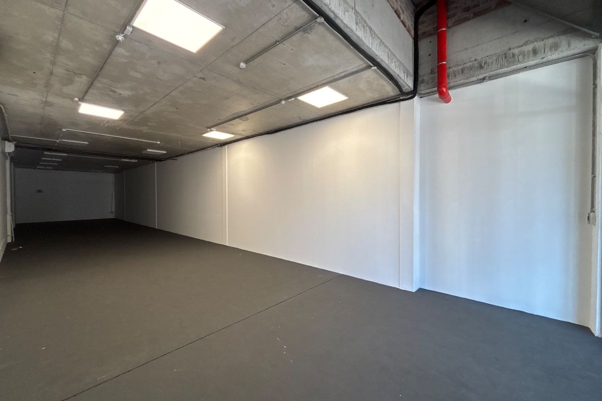 A spacious, modern open-plan retail unit featuring an industrial aesthetic with exposed concrete ceilings, recessed lighting, and clean, painted walls.