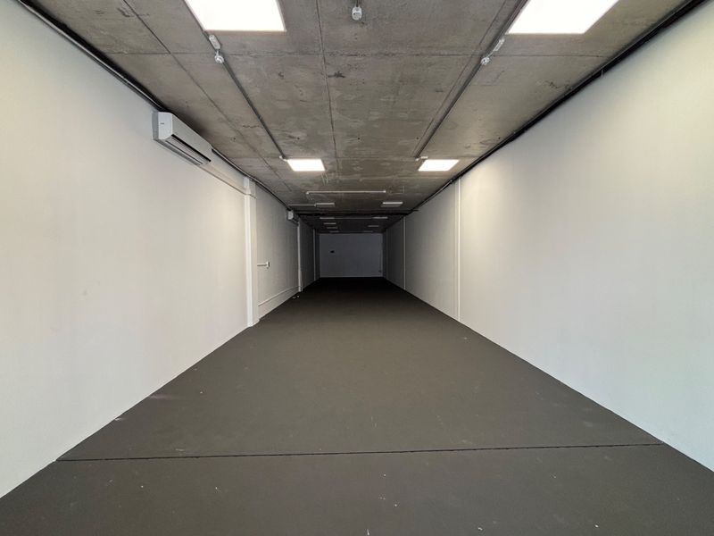 A spacious, modern open-plan retail unit featuring an exposed concrete ceiling, recessed lighting, and a wall-mounted air conditioning unit.