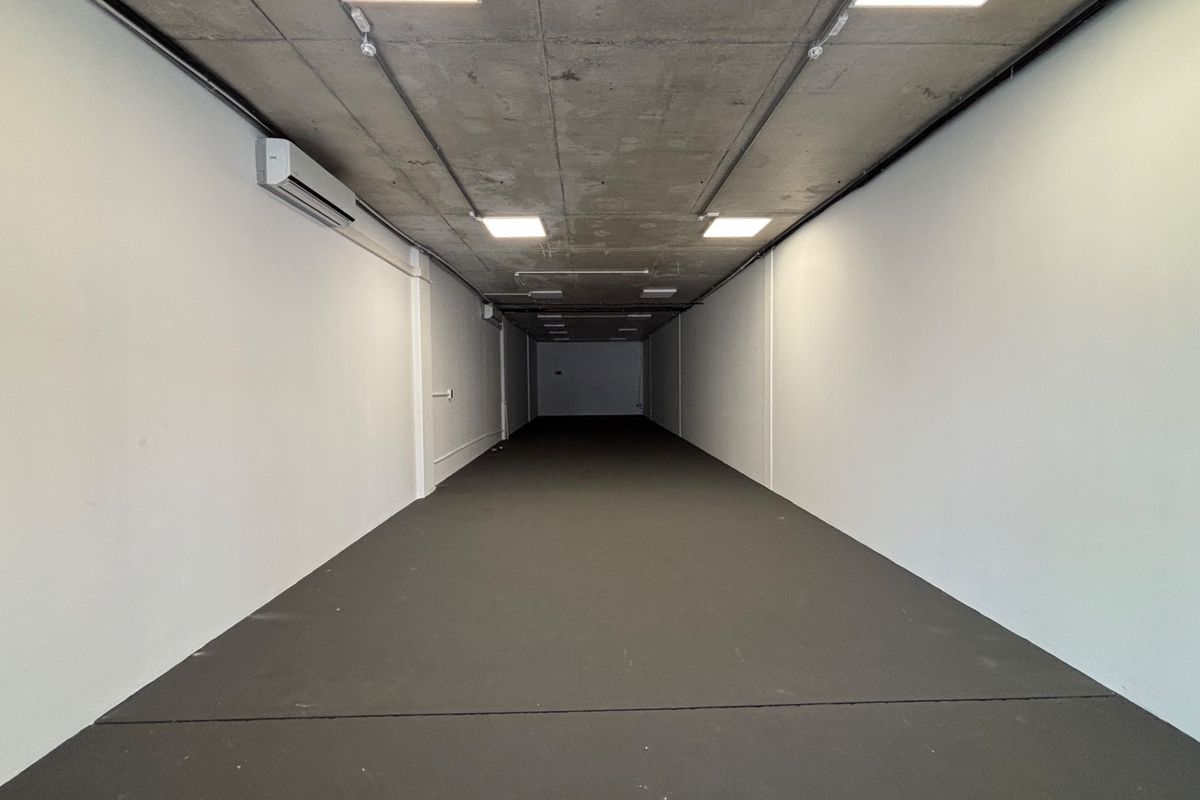 A spacious, modern open-plan retail unit featuring an exposed concrete ceiling, recessed lighting, and a wall-mounted air conditioning unit.