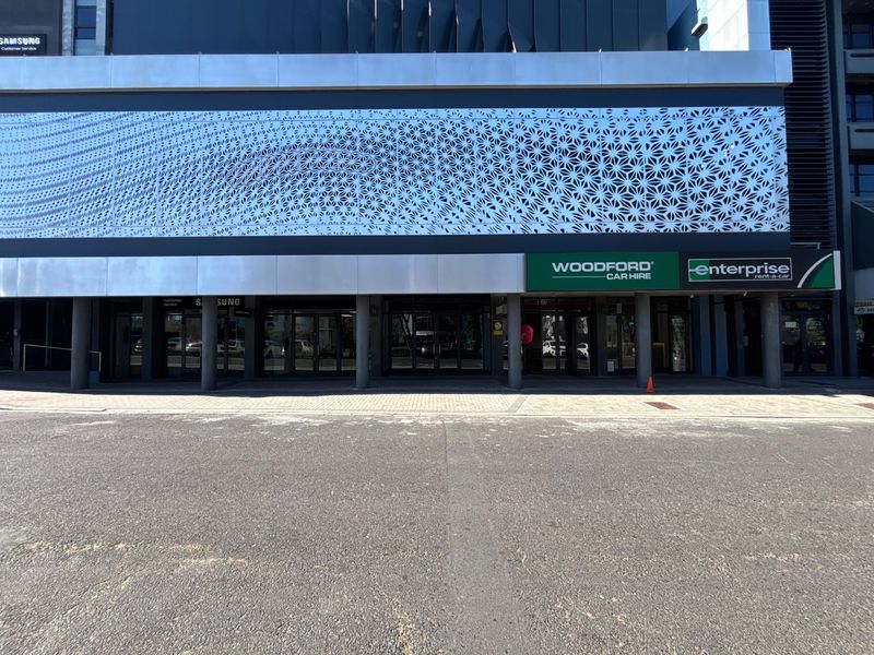 Modern commercial retail storefront featuring a decorative metal facade screen, glass entrance doors, and paved sidewalk access.