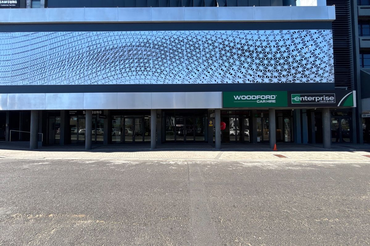 Modern commercial retail storefront featuring a decorative metal facade screen, glass entrance doors, and paved sidewalk access.