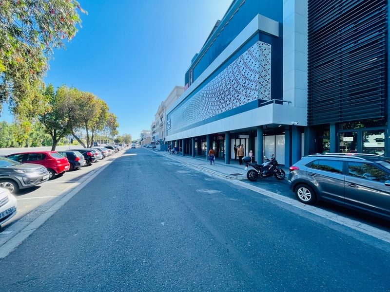 Street-level view of a modern commercial building featuring a decorative metal facade screen and a covered pedestrian walkway.