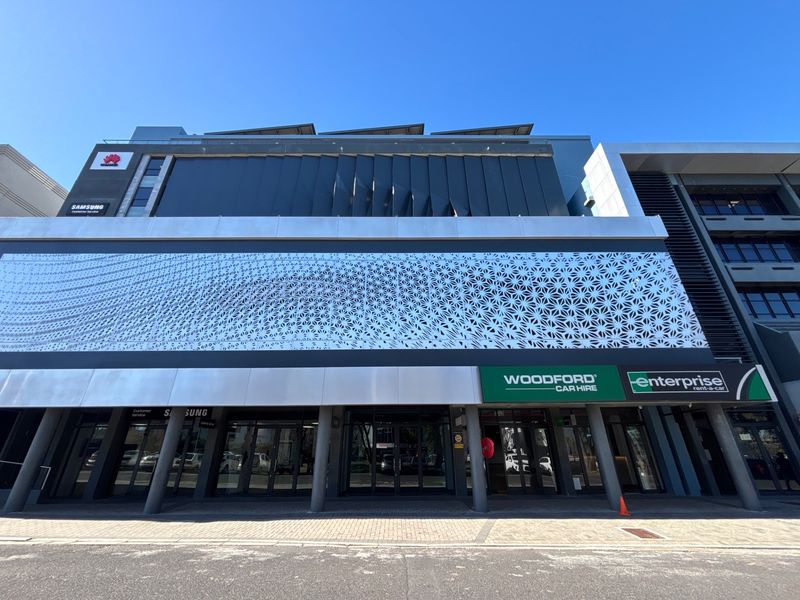 Modern commercial building facade featuring a decorative metal screen, glass storefront entrances, and integrated signage for retail tenants.