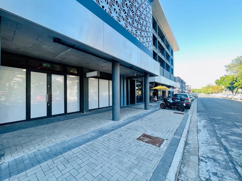 Modern retail storefront featuring a paved sidewalk, concrete structural columns, and decorative metal facade screening.