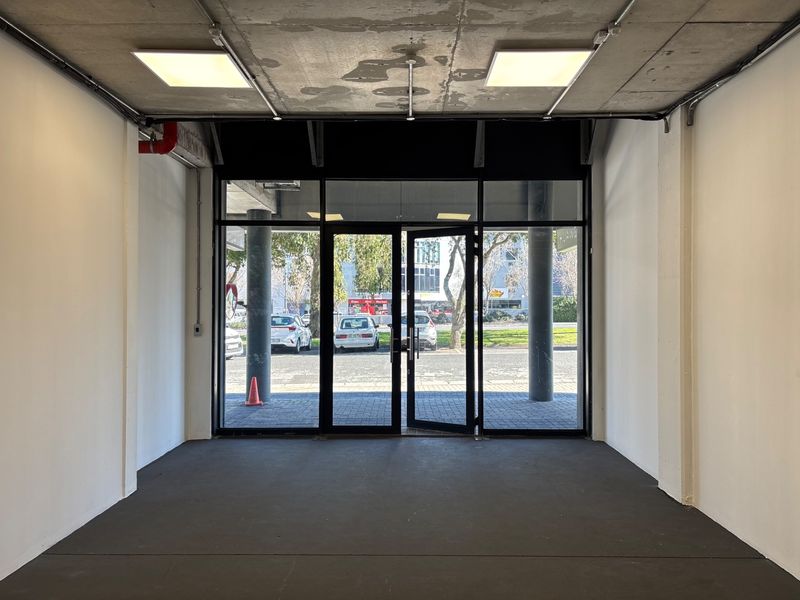 Empty retail entry space featuring an exposed concrete ceiling, glass storefront doors, and industrial-style lighting, suitable for a variety of commercial uses.