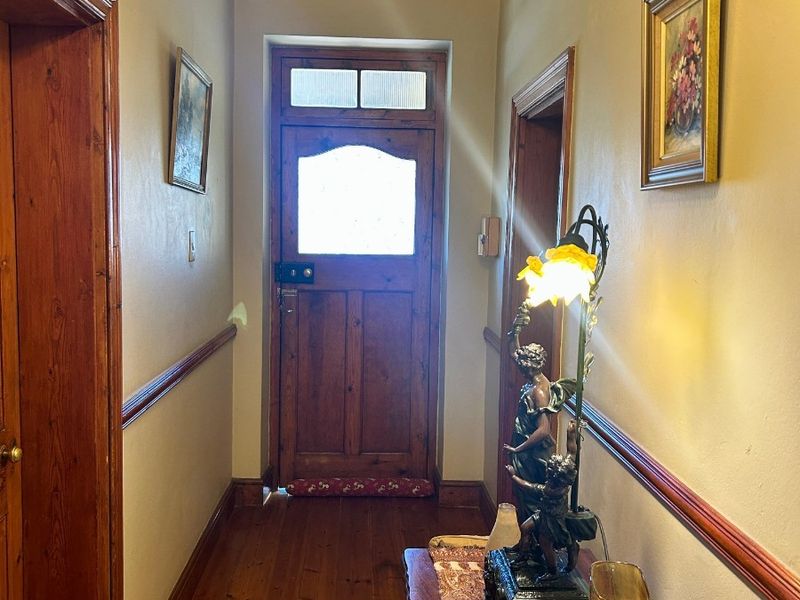 A traditional hallway featuring warm timber flooring, a solid timber entrance door with a transom window, and classic dado rail detailing.