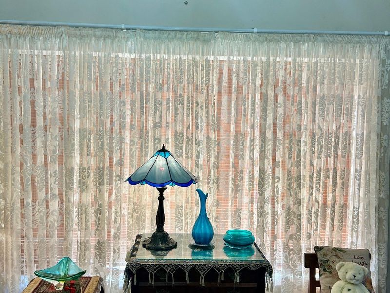 A living area featuring warm timber flooring and floor-to-ceiling sheer curtains, providing a soft, naturally lit space.