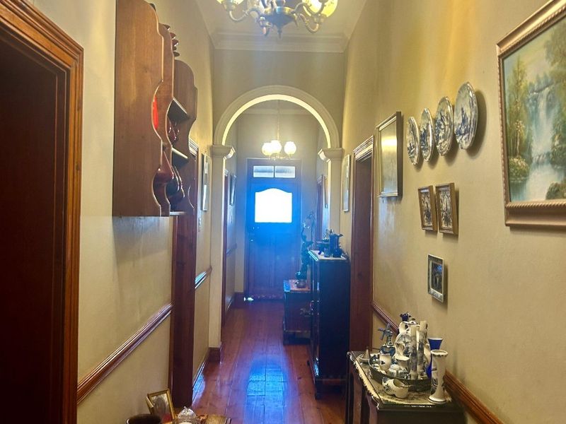 A traditional hallway featuring polished timber flooring, a decorative archway, and classic dado rail detailing, leading towards the main entrance.
