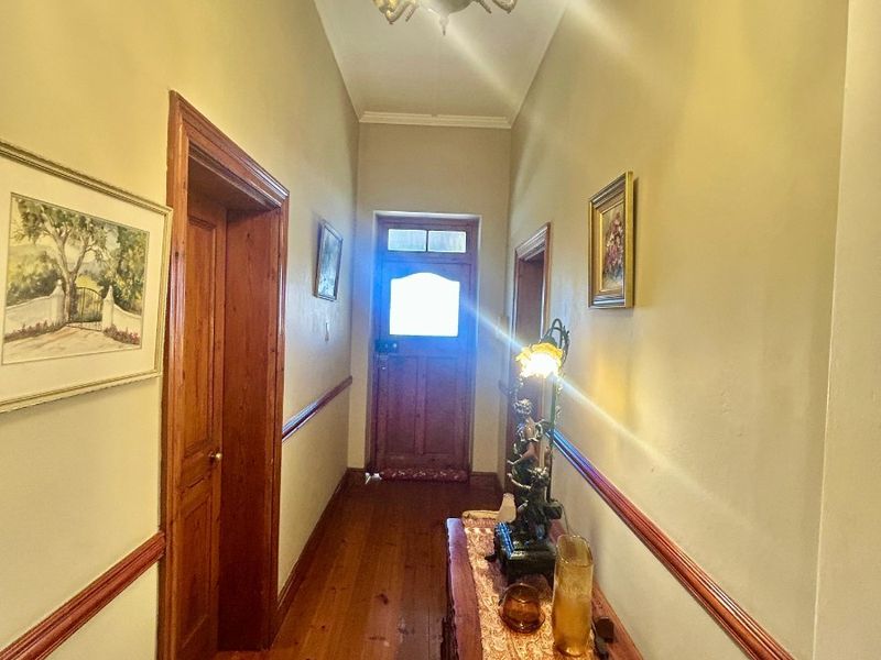 A traditional hallway featuring warm timber flooring, classic timber door frames, and a decorative chair rail, leading to an exterior entrance door.