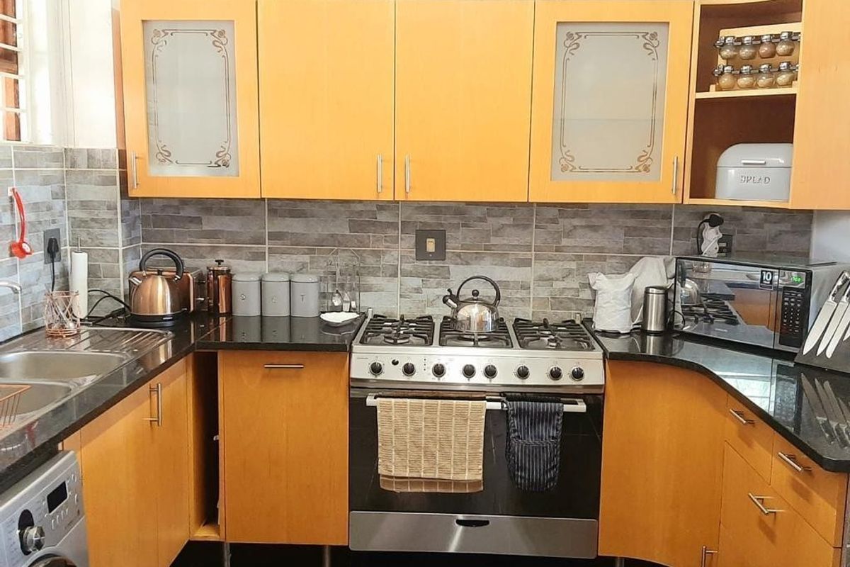 A functional kitchen featuring warm-toned cabinetry, granite countertops, a stainless steel gas stove, and a modern tiled backsplash.