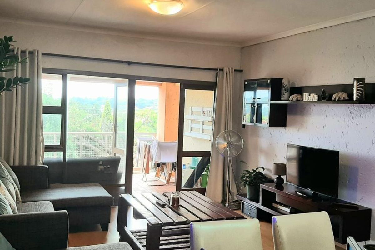 A living room featuring laminate flooring, built-in wall shelving, and a large sliding glass door providing access to an outdoor balcony area.
