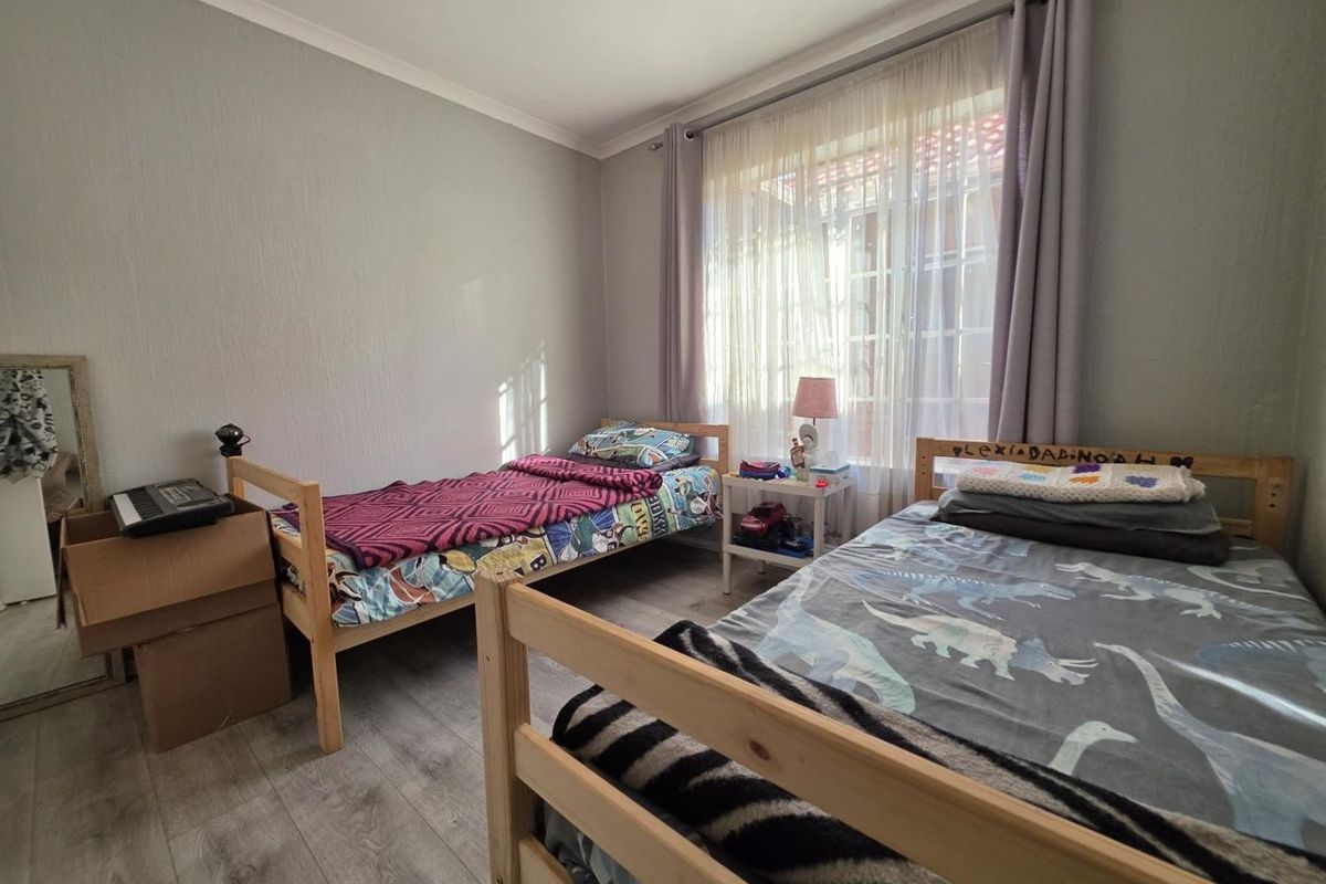 A functional bedroom featuring light-toned laminate flooring and neutral wall finishes, providing a comfortable space with natural light through the window.