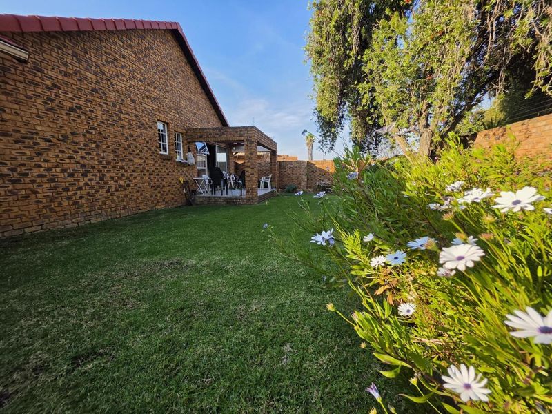 A view of the rear garden featuring a well-maintained lawn, face brick exterior walls, and a covered patio area.