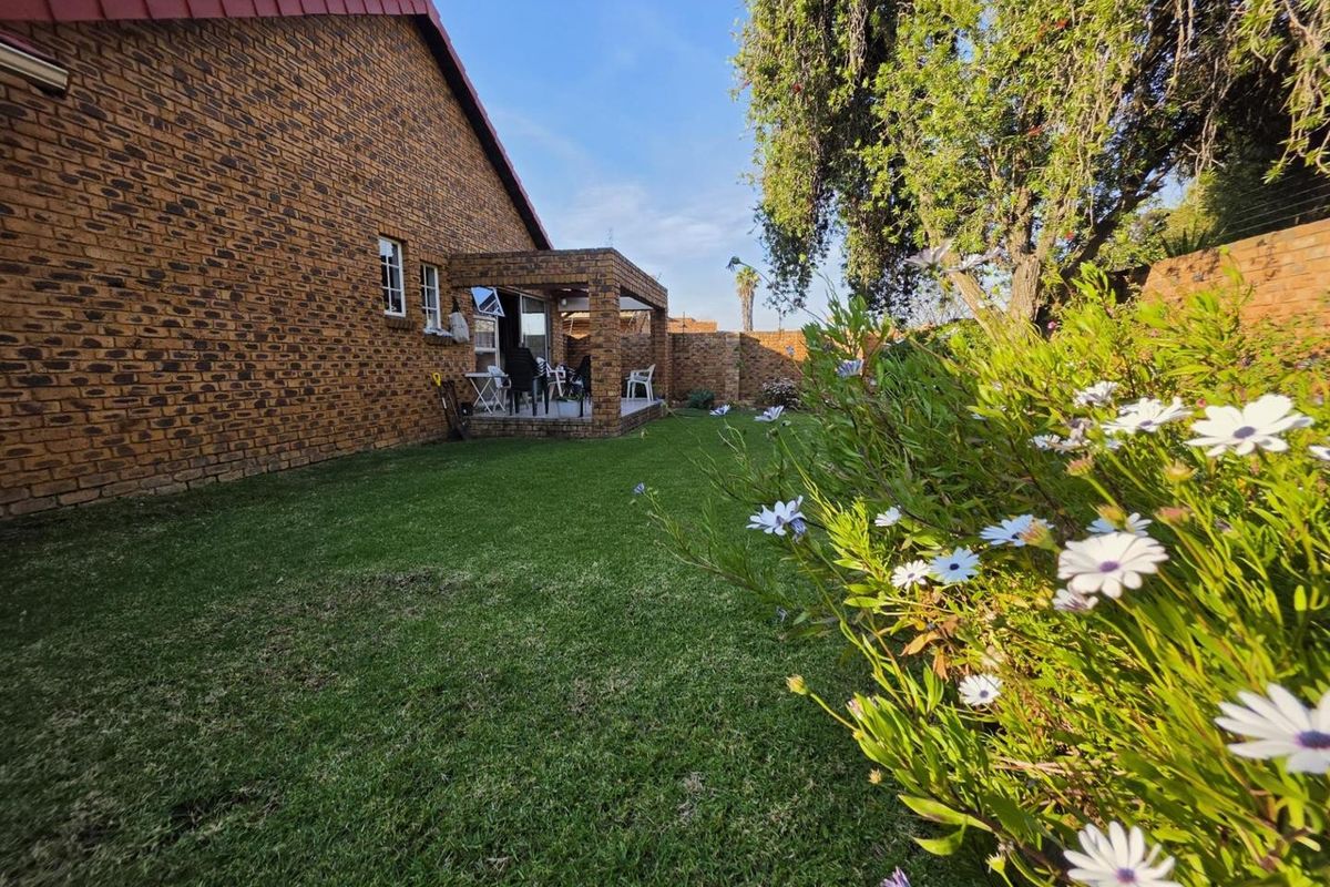 A view of the rear garden featuring a well-maintained lawn, face brick exterior walls, and a covered patio area.