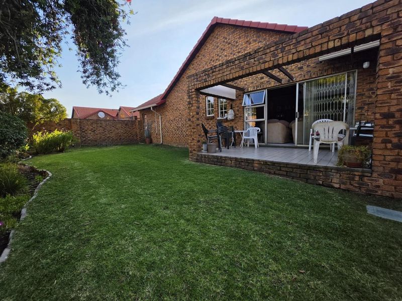 Rear view of the townhouse featuring a covered patio with tiled flooring, sliding doors, and a private garden with a lawn.