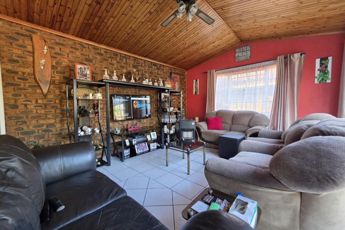 A living room featuring an exposed brick feature wall, timber-clad vaulted ceiling with a ceiling fan, and tiled flooring.