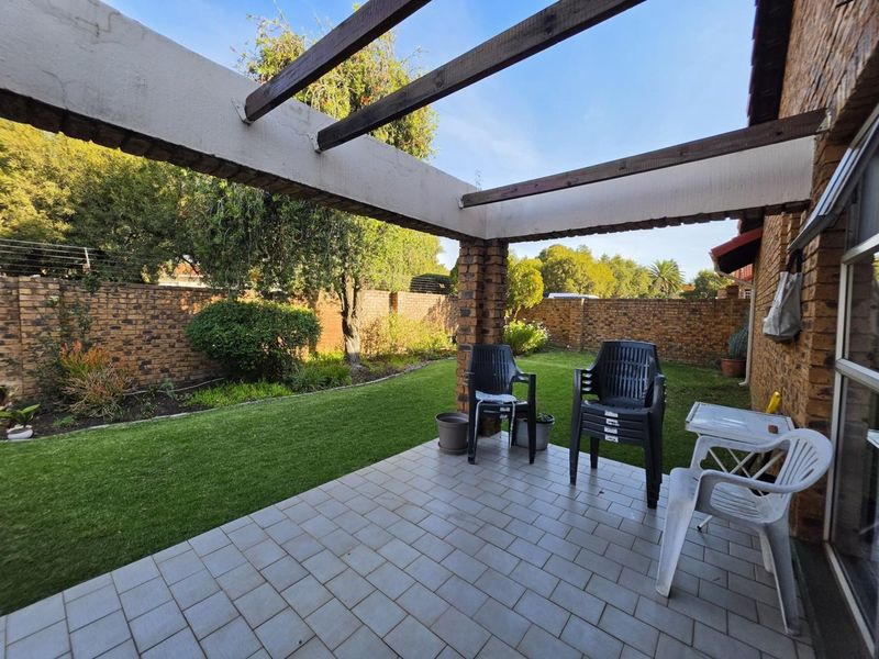 A covered patio area featuring a timber pergola, tiled flooring, and direct access to a private rear garden with brick boundary walls.